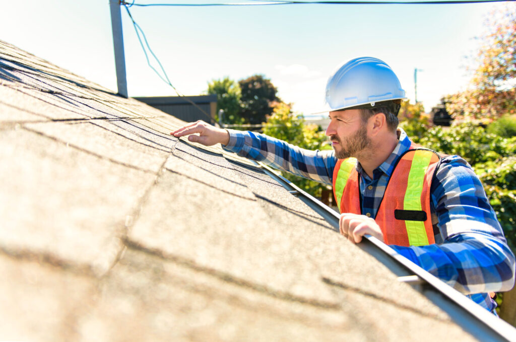 man with hard hat standing on steps inspecting house roof